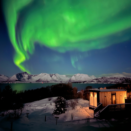 Aurora borealis over a snowy landscape with a cabin. Location is northern Norway, Lapland. 